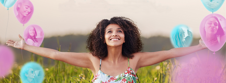 Mulher sorrindo de braços abertos com bexigas rosa e azul ao seu redor