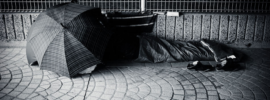 A stock photo of a homeless man sheltered under a pair of umbrellas asleep under a bridge in Tokyo, Japan