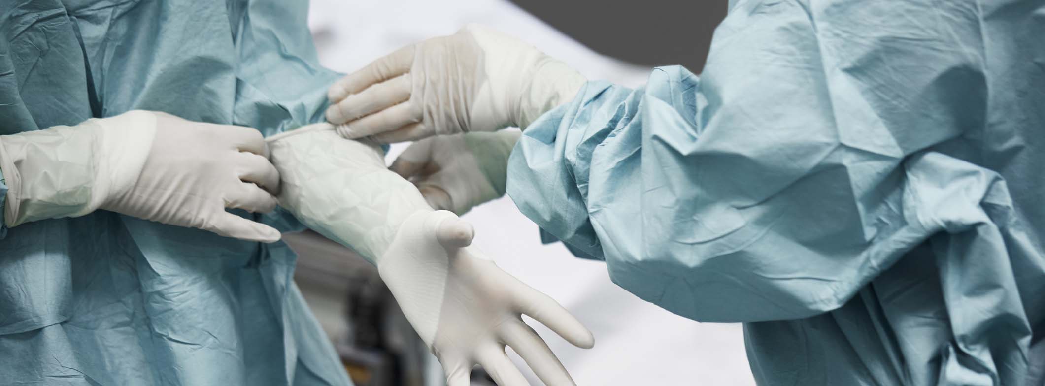 Midsection of female doctor helping surgeon wearing surgical glove. Medical colleagues are preparing for surgery. They are standing in emergency room.