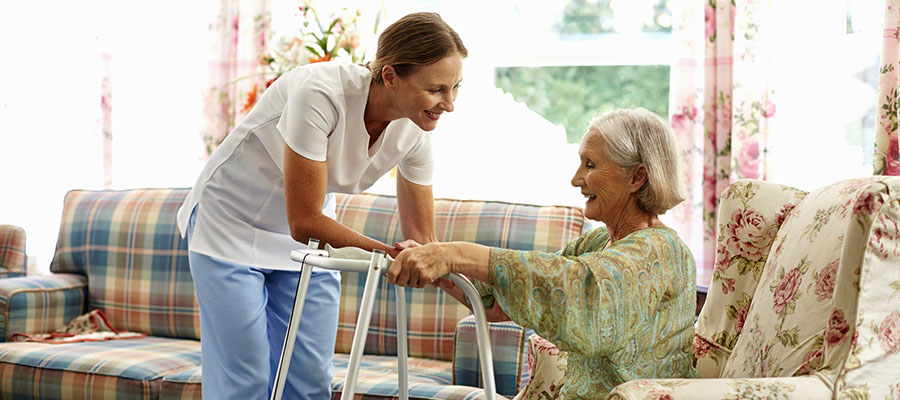 Female caretaker assisting senior woman with walker in nursing home