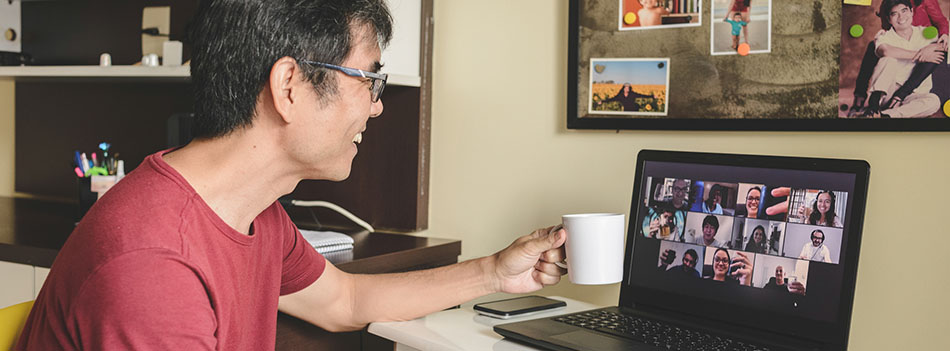 Man at home attending to a virtual happy hour with many people on screen toasting online together